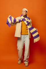 A young man with tattoos confidently poses while holding a colorful scarf in a striking setting.