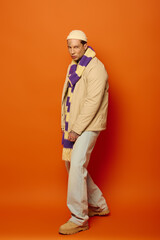 A young man flaunts his tattoos against a bright orange background in stylish attire.