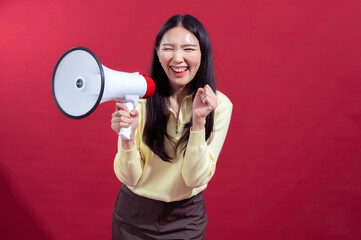 Asian woman with long black hair holding a megaphone in front, speaking enthusiastically while wearing a yellow top and brown pants, set against a vibrant red background for a bold statement