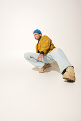 A young man showcases his tattoos while posing expressively in relaxed street style clothing.