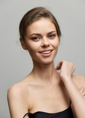 Smiling young woman with natural beauty, wearing a black strapless top. Soft gray background highlights her features. Radiating confidence and joy.