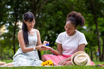 Couple of LGBTQ lesbian people having picnic in the park during summer while putting sunscreen on...