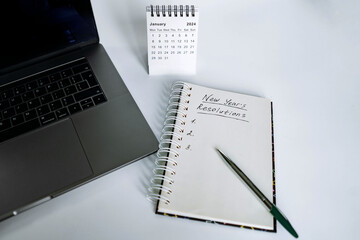 open notepad with resolutions for new 2024 year text. Near laptop, calendar and christmas tree