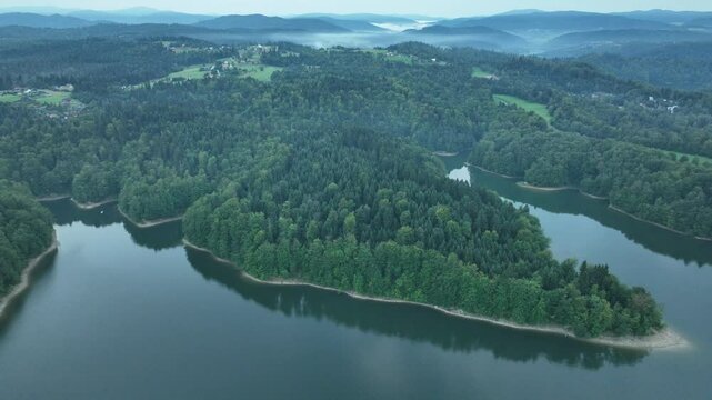 High flight over the lake surrounded by mountains with dense forest and bays. Mavic 3
