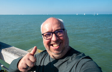 A joyful man gives an enthusiastic thumbs up by the beautiful seaside, fully enjoying a bright and...