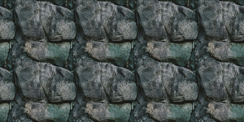 A close-up of stone with heavy weathering, with deep fissures and a blend of dark gray and greenish tones