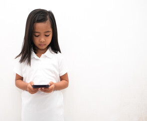 Naklejka premium beautiful asian little girl on white background holds mobile phone, uses modern cellular
