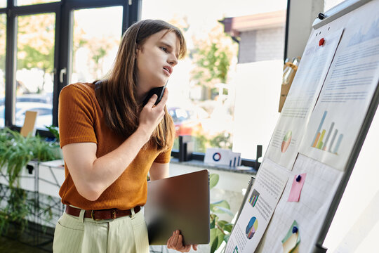 In a vibrant workspace, a non binary person reflects on charts while holding a tablet.
