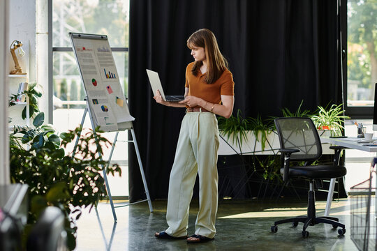 A young non binary person examines charts while standing in a modern office filled with greenery.