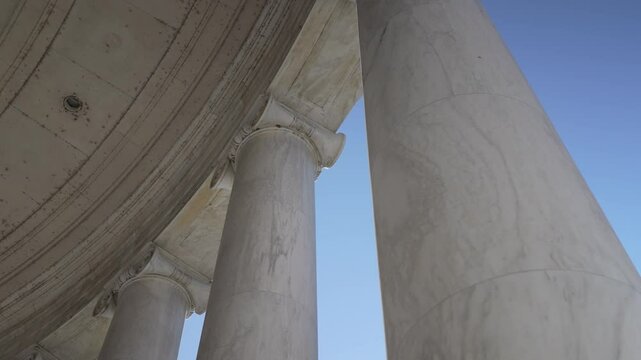 Jefferson Memorial low angle view of white marble columns reaching towards clear blue sky, the smooth texture of the stone and simplicity of scene evoking a sense of grandeur and timeless architecture