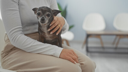A young woman holding a chihuahua in a veterinary clinic waiting room, portraying care and...