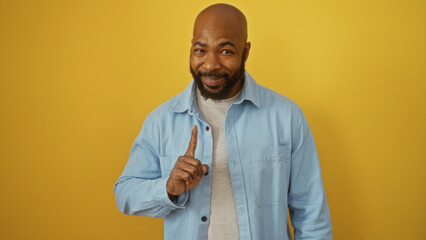 Handsome young african american man in casual attire pointing upwards against an isolated yellow...