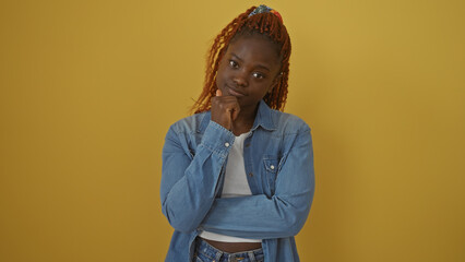 Pensive young african woman in denim over a yellow background, exuding casual style and thoughtful...