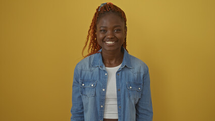 Fototapeta premium Smiling young african woman in denim jacket over isolated yellow background