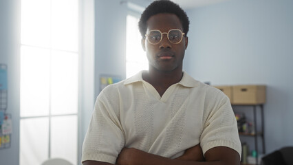 Young man standing confidently in an office with arms crossed in an indoor setting with soft...