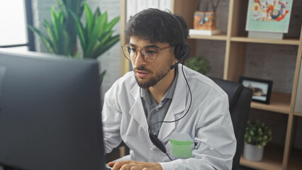 Serious arab man working on computer in medical office setting, wearing headset