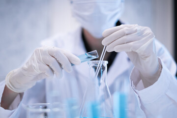 Close-up scientist pouring blue liquid into test tube beaker flask equipment pipette working...