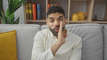 Hispanic man gesturing silence in a cozy living room with a bookshelf