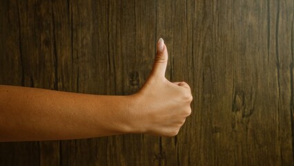 Woman's hand showing thumbs up against a wooden background, highlighting natural skin tone and positive gesture in a rustic setting