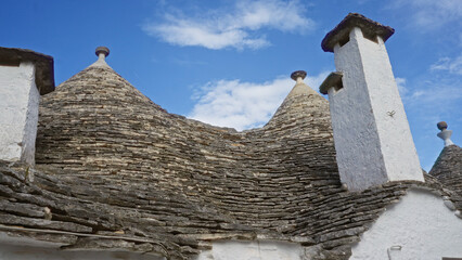 Traditional cone-roofed houses in alberobello, puglia, italy, against a vibrant blue sky showcase...