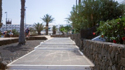 Blurred path in lanzarote with outdoor palm trees and defocused people in the background, capturing a serene sunny day in spain's canary islands.