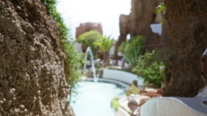 Blurred view of outdoor scenery featuring defocused elements in lanzarote, spain including natural rock formations, lush vegetation, and a swimming pool surrounded by greenery
