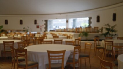 Defocused empty wedding hall with round tables and wooden chairs set up for an event