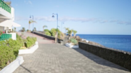 Blurred outdoor scene in lanzarote, canary islands, showing a scenic promenade with greenery, distant palm trees, and the blue ocean under a clear sky.