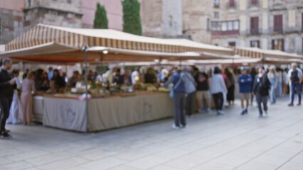 Blurred crowd browsing stalls at an outdoor vintage market in barcelona, spain, with people in focus and historic architecture in the background.
