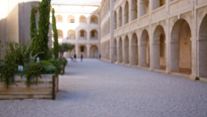 Obraz premium Blurred figures walking through outdoor university campus with historic stone arches and green foliage in defocused background creating serene atmosphere.