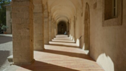 Blurred view of an old university campus corridor outdoors with stone arches and sunlight creating a defocused bokeh effect.