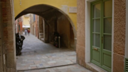 Blurred street scene in villefranche-sur-mer with stone alley, archway, and pastel facades under soft daylight, evoking the charm of an old french town.