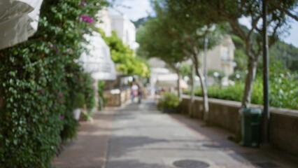 Obraz premium Blurred view of a picturesque street on capri island with lush greenery and distant figures under clear skies, capturing the essence of luxury and tranquility.