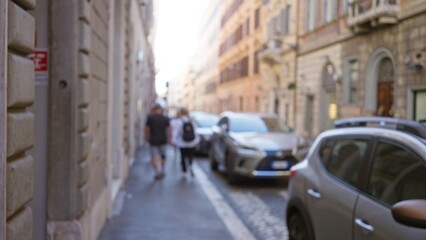 Blurred image captures a couple walking on a historic street in rome, italy, with cars parked alongside and an out-of-focus vintage architecture creating a bokeh effect.