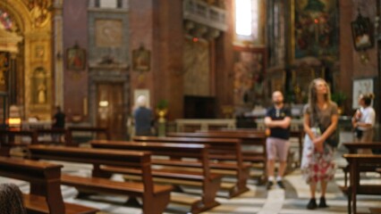 People standing indoors in a blurred, out of focus church setting with benches and religious artwork in the background, capturing a calm, contemplative atmosphere.