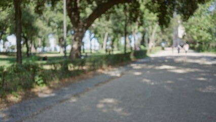 Fototapeta premium Blurred view of people walking in the sunlit villa borghese gardens in rome, showcasing green trees and paths with an out-of-focus, bokeh effect.