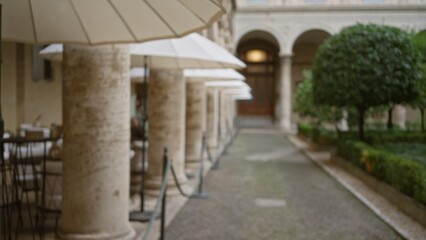 Fototapeta premium Blurred courtyard scene with columns and umbrellas creating a serene garden atmosphere, showcasing an elegant outdoor patio with bokeh effect.