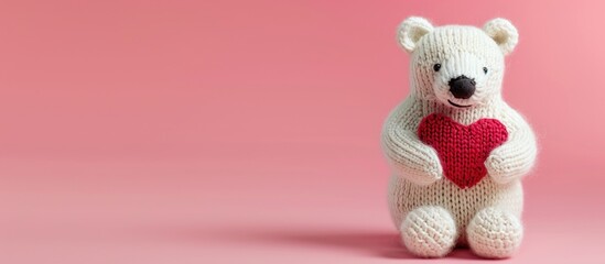 Fototapeta premium Adorable knitted polar bear toy clutching a red heart against a pink backdrop with room for text in the image. Copy space image. Place for adding text and design