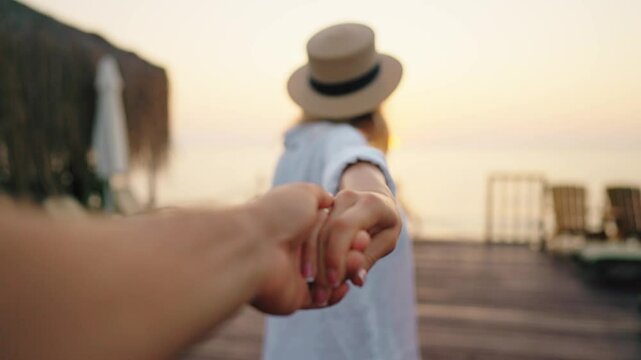 Happy woman leading her boyfriend or husband to sea, following shot, hold hand. Travel to sea or ocean, sunset or sunrise above horizon, start of day, trip to coastline, slow motion, lovers traveling