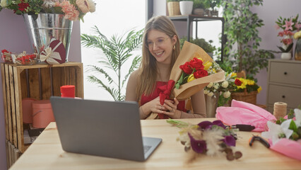 A smiling young woman enjoying a video call holding a bouquet of red roses in a vibrant flower shop