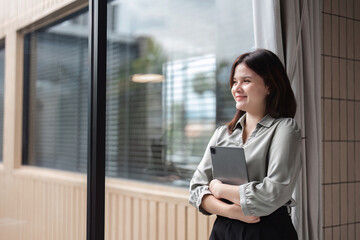 Fototapeta premium Confident Businesswoman Holding Tablet in Modern Office Setting with Natural Light and Professional Attire