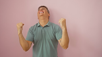 Young man celebrating with raised fists in front of an isolated pink background, expressing...