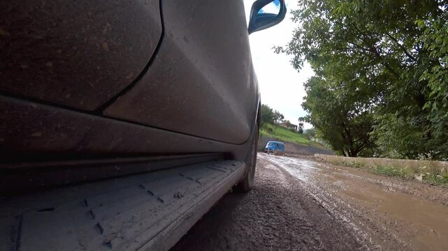 Black car driving on muddy road in mountains. Road is bumpy, and there are stones on side. Driver carefully navigates in difficult terrain. View of camera from roof of car.