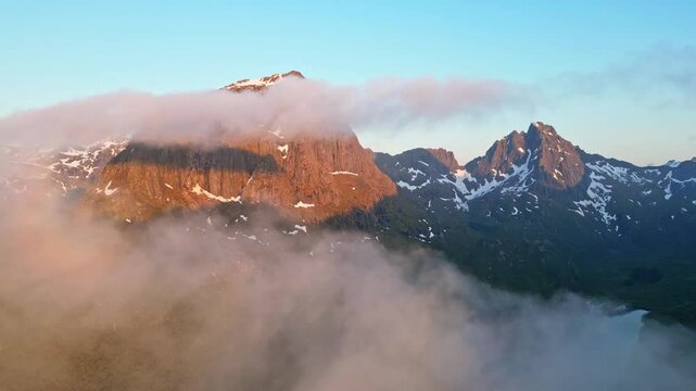 Aerial view of majestic mountains shrouded in clouds and fog under the midnight sun, Hanoy, Norway.