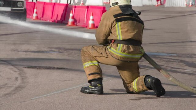 Fireman Fights Fire. An unrecognizable firefighter in a protective fireproof suit directs a stream from a fire hose to the left