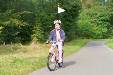 Little cute girl in glasses and helmet riding a bicycle on a path in the park. Concept of...