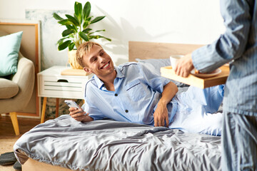 A joyful gay couple enjoys a leisurely morning in their pajamas, sharing warmth and affection in bed.