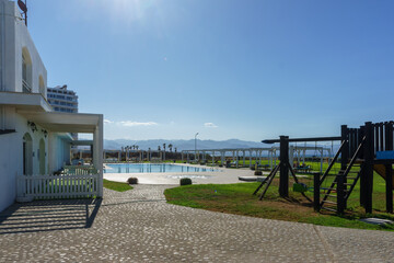 A serene afternoon at a coastal resort featuring a pool and playground under a clear blue sky.