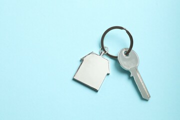 Metallic key with keychain in shape of house on color background