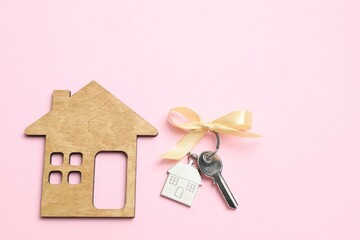 Metallic key with keychain and wooden house on color background
